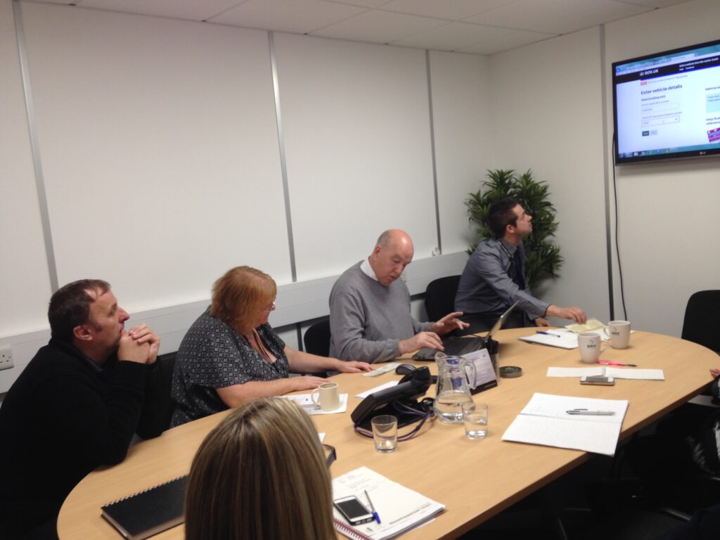 4 motor traders sitting at a table looking at a presentation on a TV monitor