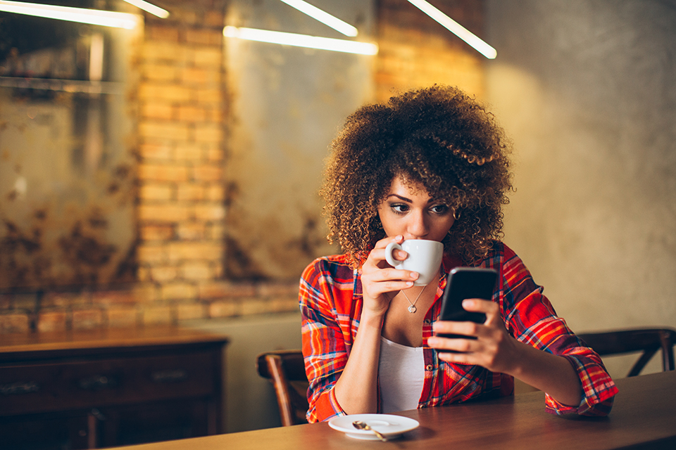 Woman sitting drinking coffee and using mobile phone