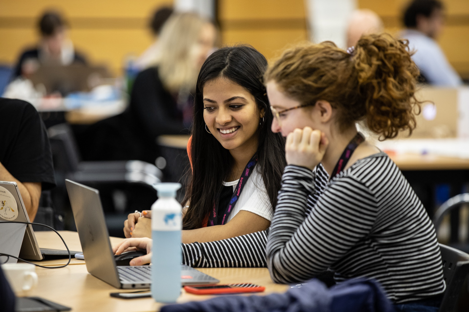 2 girls sitting at a desk looking at a laptop