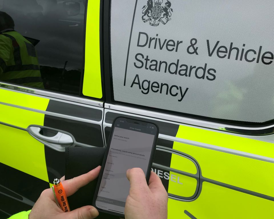 Enforcement officer using his phone next to a Driver and Vehicle Standards Agency vehicle.