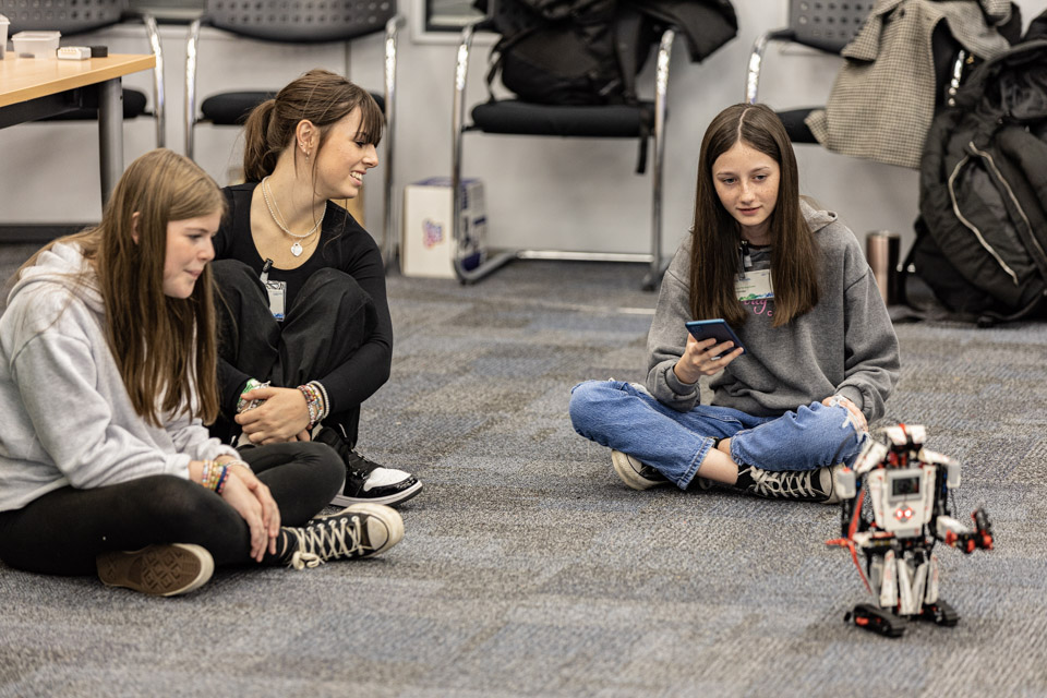 3 girls sitting on the floor playing with a robot.